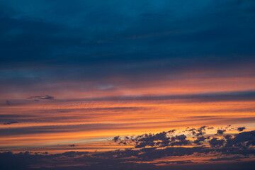 Colors blend beautifully in the sky as the sun rises, casting warm tones of orange and yellow through fluffy clouds.