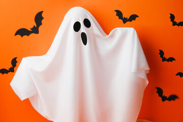 White fabric ghost with surprised face and black bats on orange background