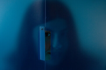 Young woman peeking out from behind a blue panel, ideal for creative campaigns.Artistic picture of...