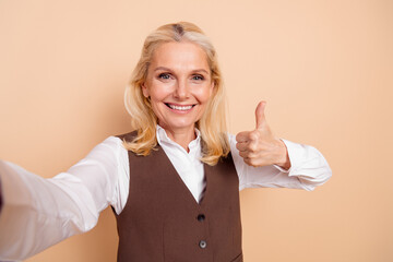Portrait of a confident middle-aged businesswoman in formal attire giving a thumbs up, showing...