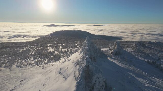 Aerial view along a sharp winter arete at Sheregesh, the sun over a valley filled with clouds while the drone tracks the ridge toward distant peaks. Strong contrast and long shadows emphasize depth