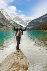 Lake Louise, Canada: A cheerful hiker stands triumphantly on a lakeside rock, celebrating stunning mountain views and the vibrant turquoise waters.