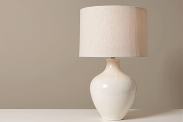 Elegant and simple white ceramic table lamp with a fabric lampshade providing cozy light in a minimalist home interior with a neutral wall