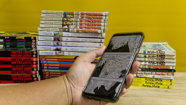 Kalimantan Selatan, Indonesia - 09 11 2025 : Person reading Boruto manga digitally with stack of Japanese comic books in background, highlighting modern comic culture.