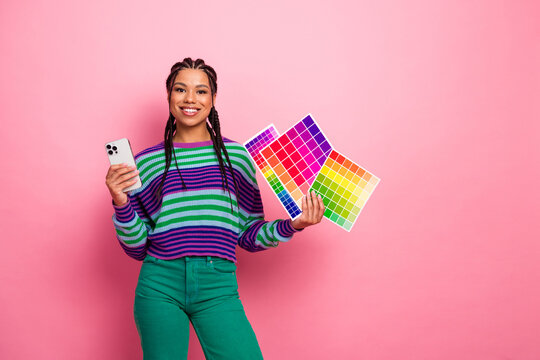 Young stylish woman with braided hair holding color samples and smartphone against vibrant pink background - Powered by Adobe