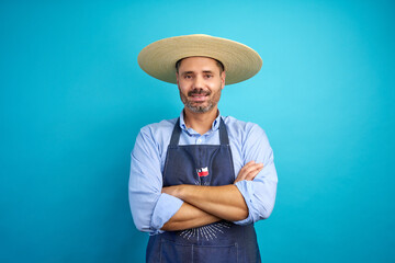 Portrait of a cheerful chilean farmer wearing a straw hat chupalla and apron, standing with crossed...