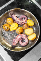 Pan-fried octopus tentacles with golden potatoes in a metal skillet. Rustic seafood dish with bubbling oil, cooked on stovetop. Mediterranean-style home cooking