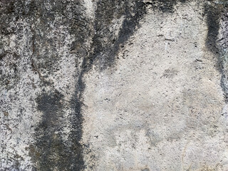 A detailed, high-resolution shot captures the rough, textured surface of a weathered concrete or stucco wall. The image reveals streaks of dark black and brown dirt and grime.