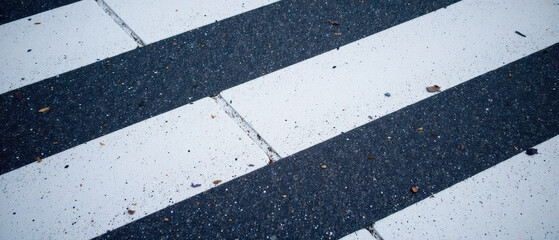Fototapeta premium Crosswalk pavement with black and white stripes, showing texture and small debris. scene conveys sense of urban life and movement