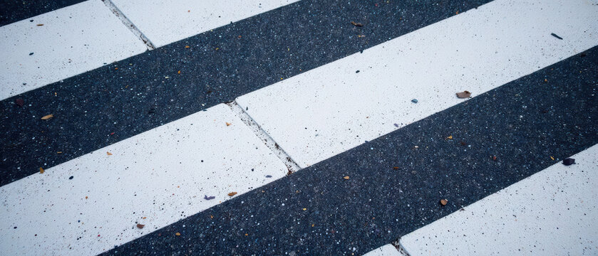 Crosswalk pavement with black and white stripes, showing texture and small debris. scene conveys sense of urban life and movement
