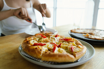 woman enjoys a freshly baked pizza with cheese, crab sticks and pineapple on a wooden table, ready to be served.