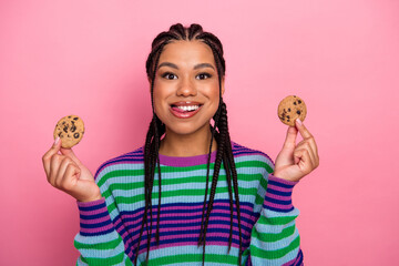 Cheerful young woman with braided hair holding cookies against a pink background and expressing joy