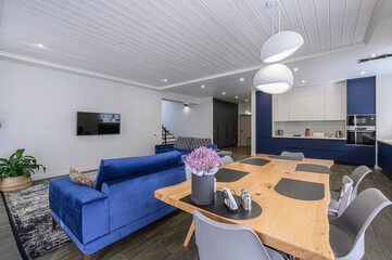 modern living space with a blue sofa, wooden table, and a sleek kitchen area featuring blue and white cabinets. The interior design is stylish and contemporary