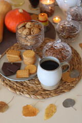 Lit candles, cookies, chocolate, nuts, tea, wine, pumpkins, books, reading glasses and autumn leaves on the table. Autumnal hygge at home. Selective focus.