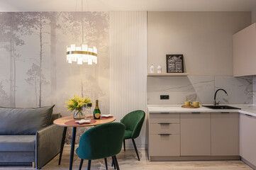 cozy apartment interior featuring a dining area with a round table, two green chairs, a sofa, and a kitchen area in neutral tones
