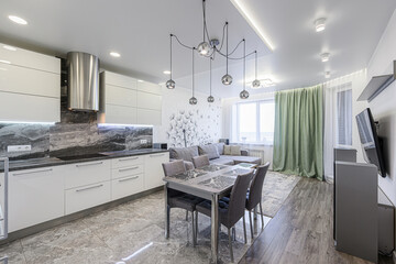 Modern apartment interior with white kitchen, dining area, gray sofa, and dandelion wall decor. Stylish lighting and gray accents throughout