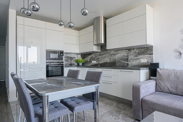 Modern kitchen with white cabinets, marble backsplash & table, and gray chairs. Chrome accents add a sleek touch