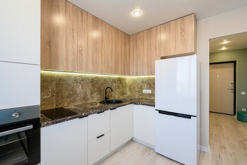 A modern kitchen features white cabinets, wood-paneled upper cabinets, and a marble backsplash. A black sink and appliances add contrast