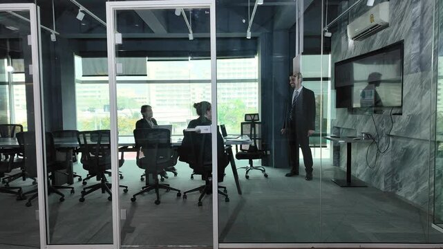 Modern Corporate Meeting Room: Business professionals engage in discussion around a conference table in a sleek, modern office meeting room with glass partitions.