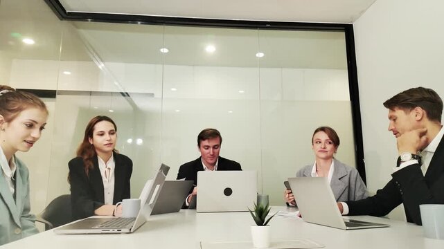 Boardroom Collaboration: A group of business professionals in a modern boardroom engage in a meeting, with laptops open and discussions underway.