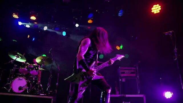 Dynamic low-angle shot of a rock guitarist on stage, bathed in colorful lights and smoke, capturing the energy of a live concert video.