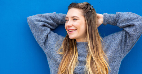 Closeup smiling woman standing against blue wall with hands behind head
