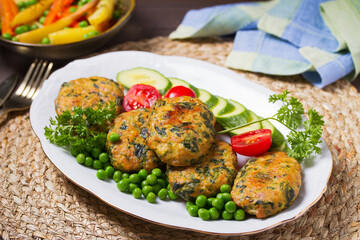 Chicken spinach burgers with green peas and vegetables on white plate