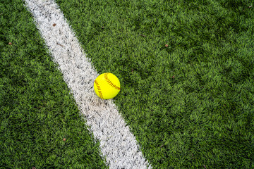 A vibrant neon yellow softball rests directly on a thick, On the Line: A Yellow Softball Poised for Action