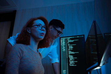 Two software developers collaborating at night, focusing on code review and debugging process on a computer screen, representing teamwork, innovation, and modern software development workflow.