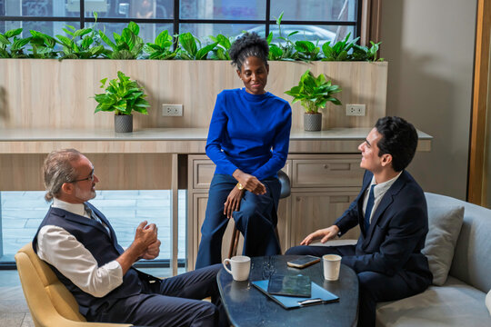 Group of diverse business professionals having a casual meeting in a modern office lounge. Ideal for teamwork, communication, leadership, and corporate diversity concepts.