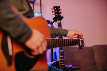 Musician tuning acoustic guitar at home studio