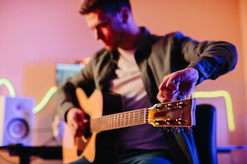 Musician tuning acoustic guitar and writing music at home studio