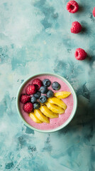 A pink smoothie bowl topped with raspberries, blueberries, and mango slices on a textured teal background, with scattered raspberries nearby.