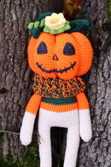 A cuddly crocheted stuffed animal dressed as a pumpkin for Halloween or fall celebrations