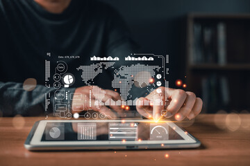 A person interacts with a digital tablet displaying futuristic data visualization overlays including charts,maps,and analytics icons representing global technology,statistics,and big data insights.