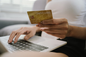 A young woman uses her smartphone and holds credit cards while sitting indoors, representing online shopping, finance, technology, and e-commerce.
