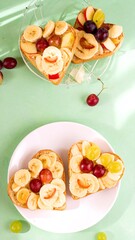 Two heart-shaped toasts, topped with vibrant slices of banana, red grapes, and , create a delightful and colorful breakfast or snack.