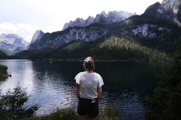 Mujer viendo montañas y lago.Young hiker girl sitting on a bench, overlooking stunning lake and...