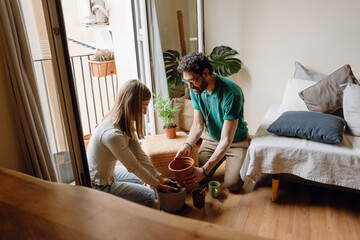 A man holds a flowerpot while a woman sits next to him on the floor holding soil
