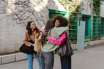 Two female friends stand and hug while a female friend stands next to them and laughs