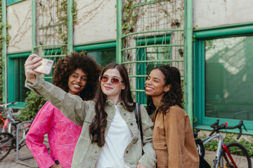 A group of three female friends smiling and posing while looking at a phone held by one of them