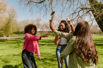 Fototapeta premium A group of three female friends are dancing and laughing while one of them is holding a phone
