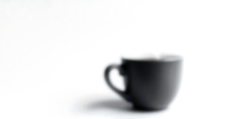 Obraz premium A blurred image of a dark-colored cup with a handle, set against a bright, white background.