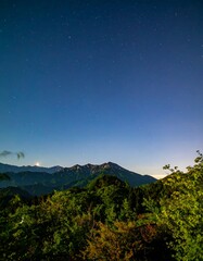 Starry night over mountain peaks. Lush forest at base