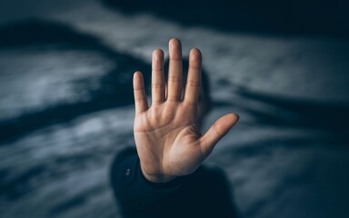 Closeup of a hand held up in a stop gesture against a dark, blurred background, conveying a message of prohibition or warning