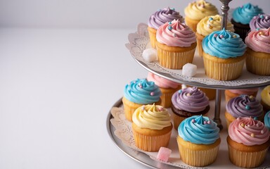 A tiered silver stand displaying an assortment of colorful cupcakes with swirled frosting and sprinkles, set against a white background