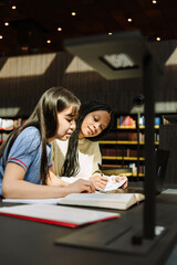 Two female students sit at a table and look at a book while holding pens