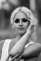 Naklejka premium Portrait of a beautiful blonde girl in a white tunic in a forest park. Black and white photo.