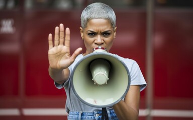 A determined woman with short gray hair speaks into a megaphone, holding up her hand in a stop gesture