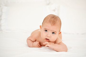 A baby boy in diapers on a white bed in a bedroom, a cute little baby of six months, a place for text